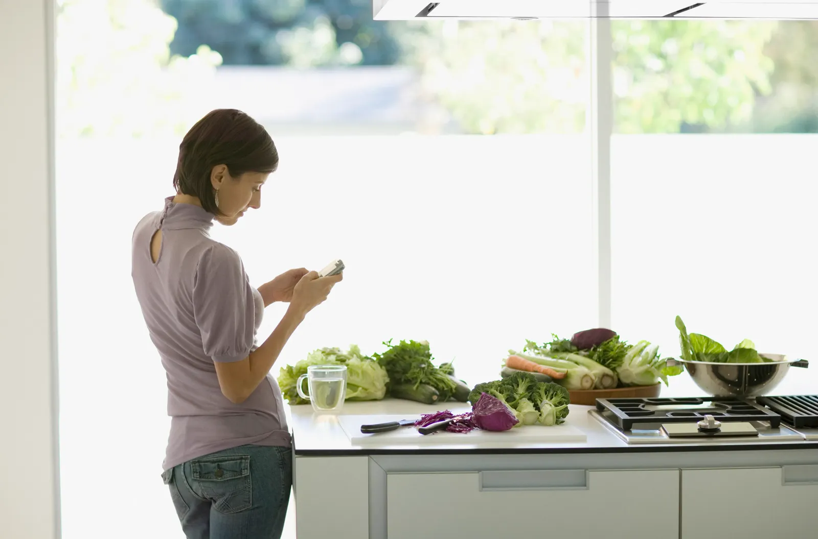 Woman in a bright kitchen pouring a glass of water — the minerals in your water are a small daily habit that compounds over years, which is why WHO's research focuses on long-term, sustained intake rather than any single glass