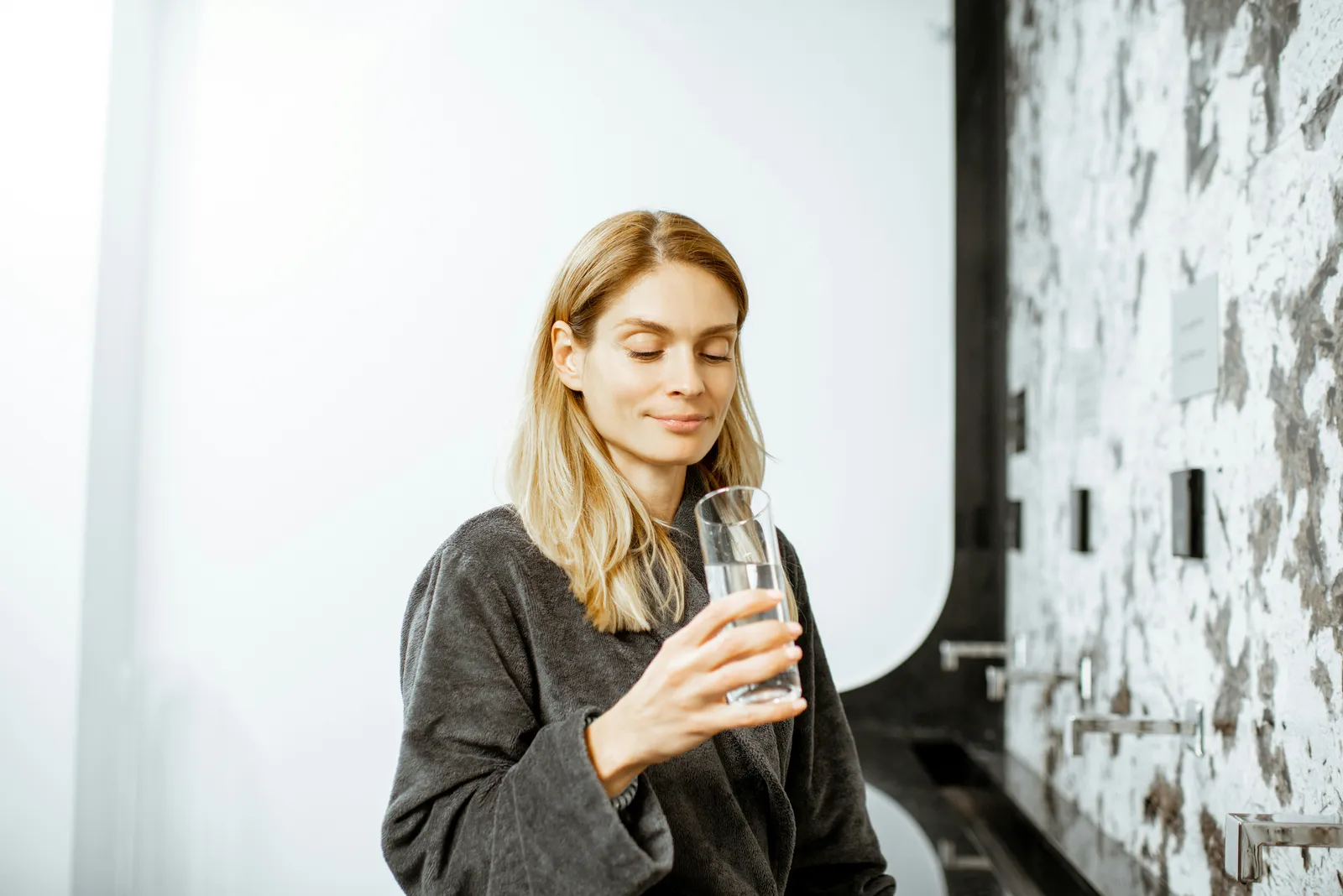 Woman calmly drinking a glass of water at home — filtration cannot fix hormones, but it can remove the documented endocrine disruptors that are one of the few variables you actually control