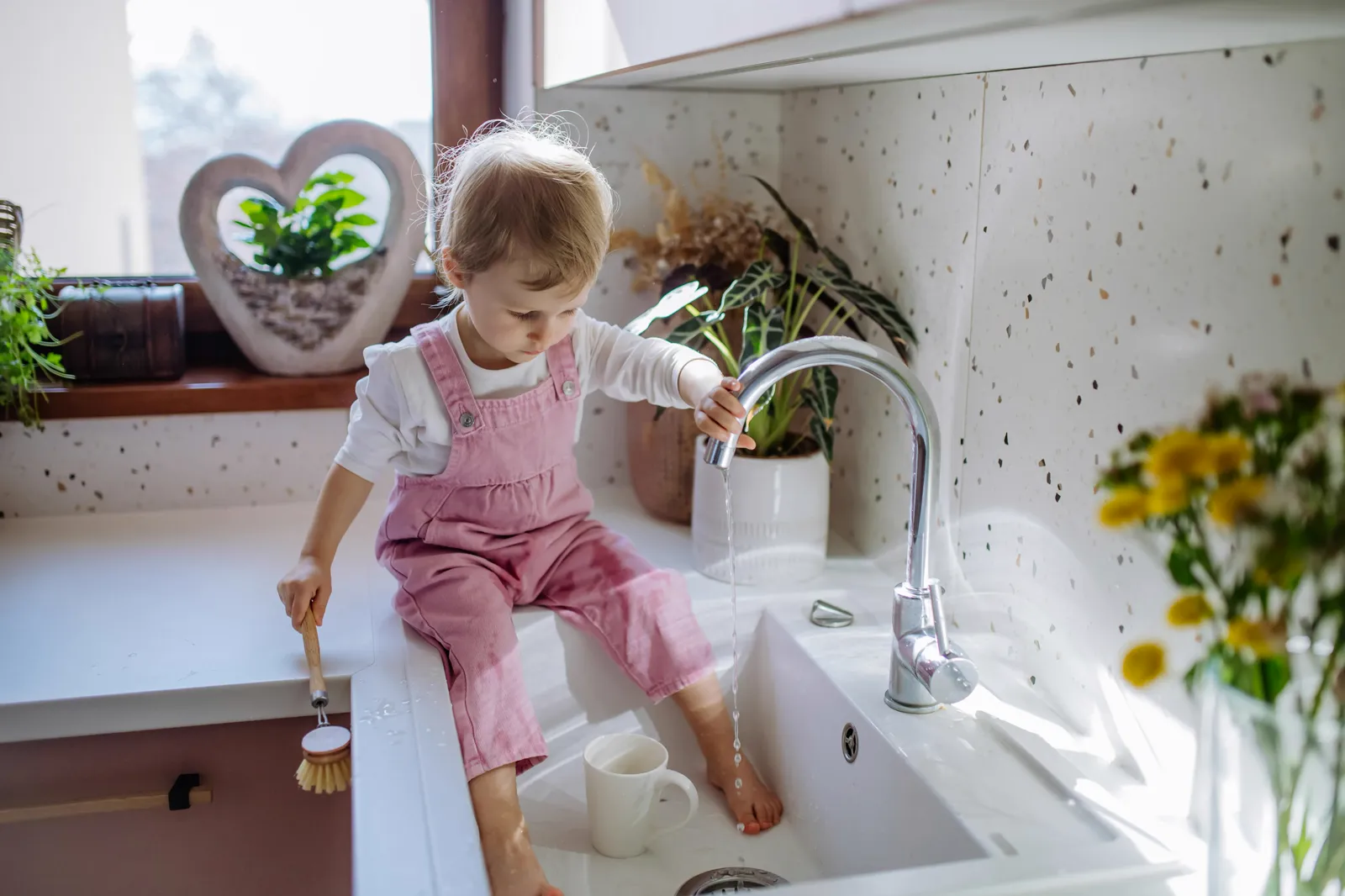 Child reaching up to turn on kitchen faucet — regular filter replacement is what keeps the water coming out of that tap clean