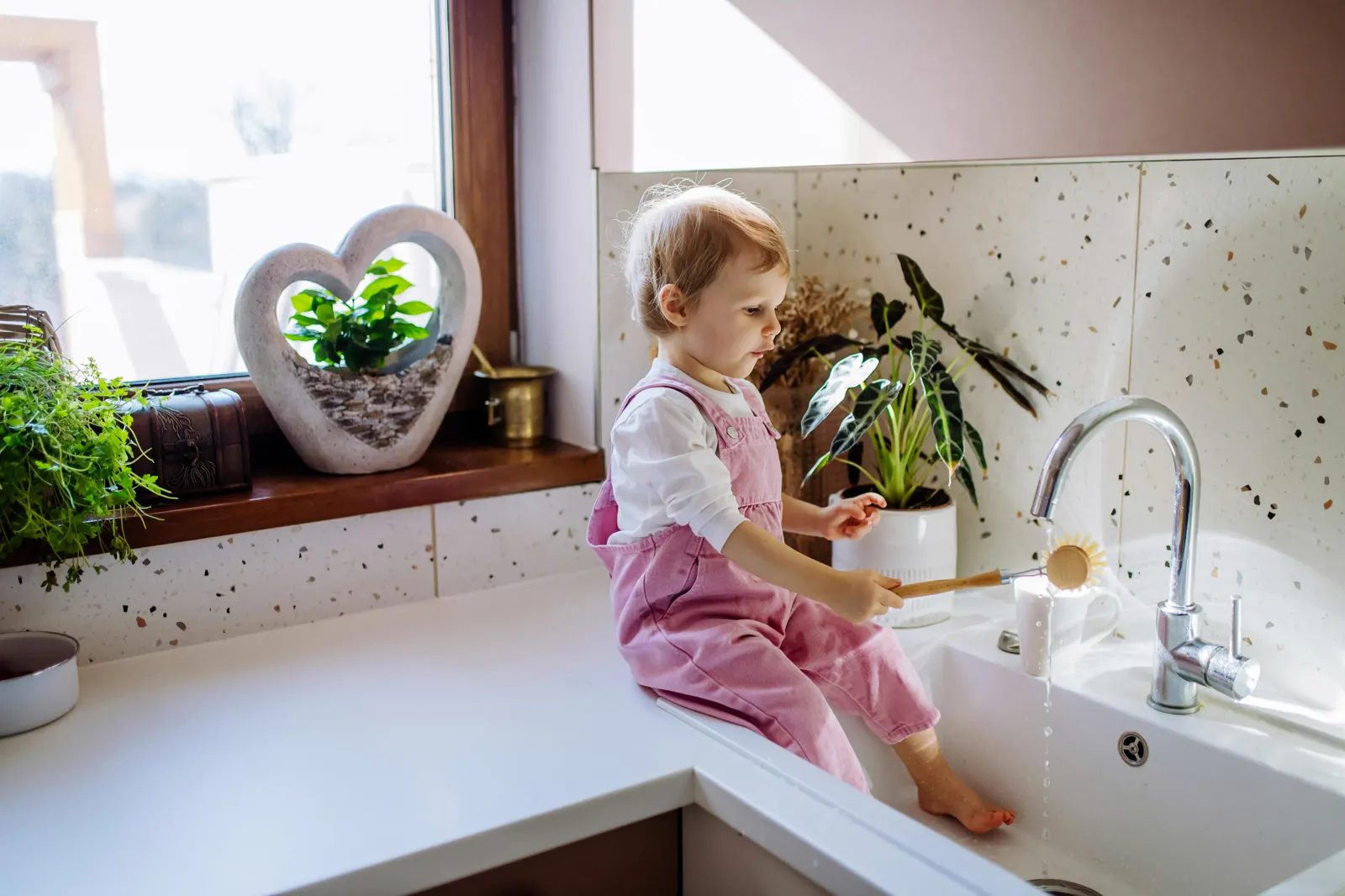 Toddler at kitchen sink while parent washes dishes — regular filter maintenance protects the whole family's drinking water