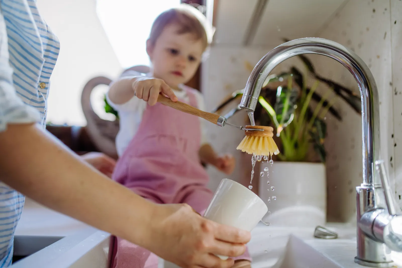Parent and toddler washing dishes at a kitchen sink — hard water affects every water-using task and appliance in the home