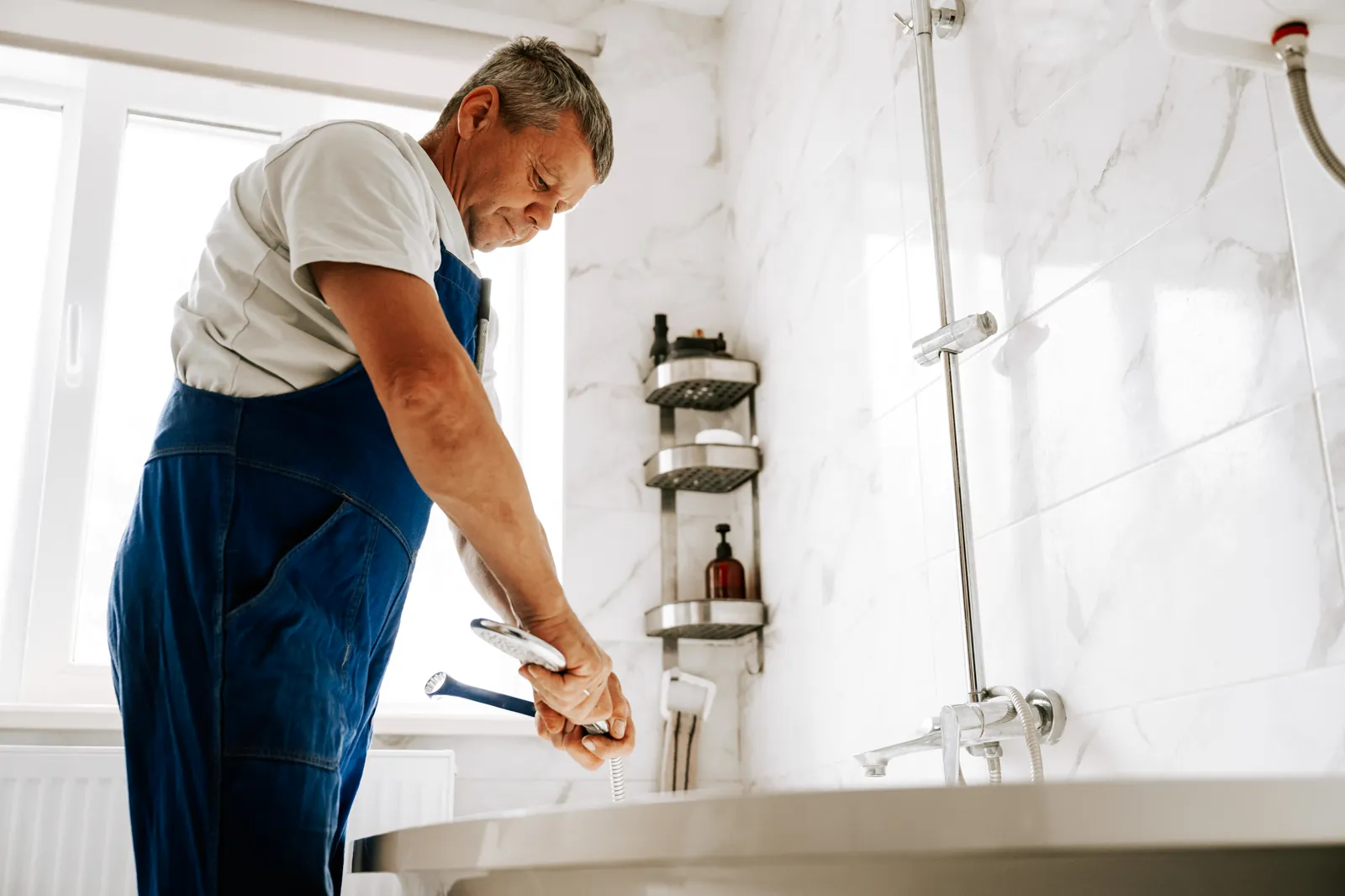 Plumber in blue overalls working on a bathroom fixture — hard water scale buildup is a common cause of plumbing and fixture maintenance calls