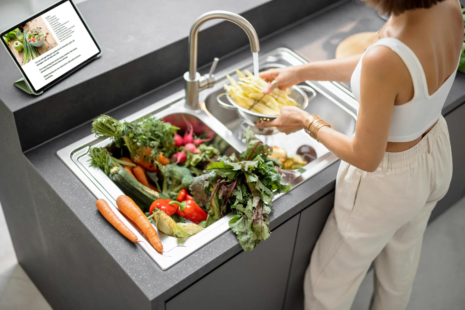 Person washing fresh vegetables at a kitchen sink with clean filtered water — the everyday result of effective home water filtration