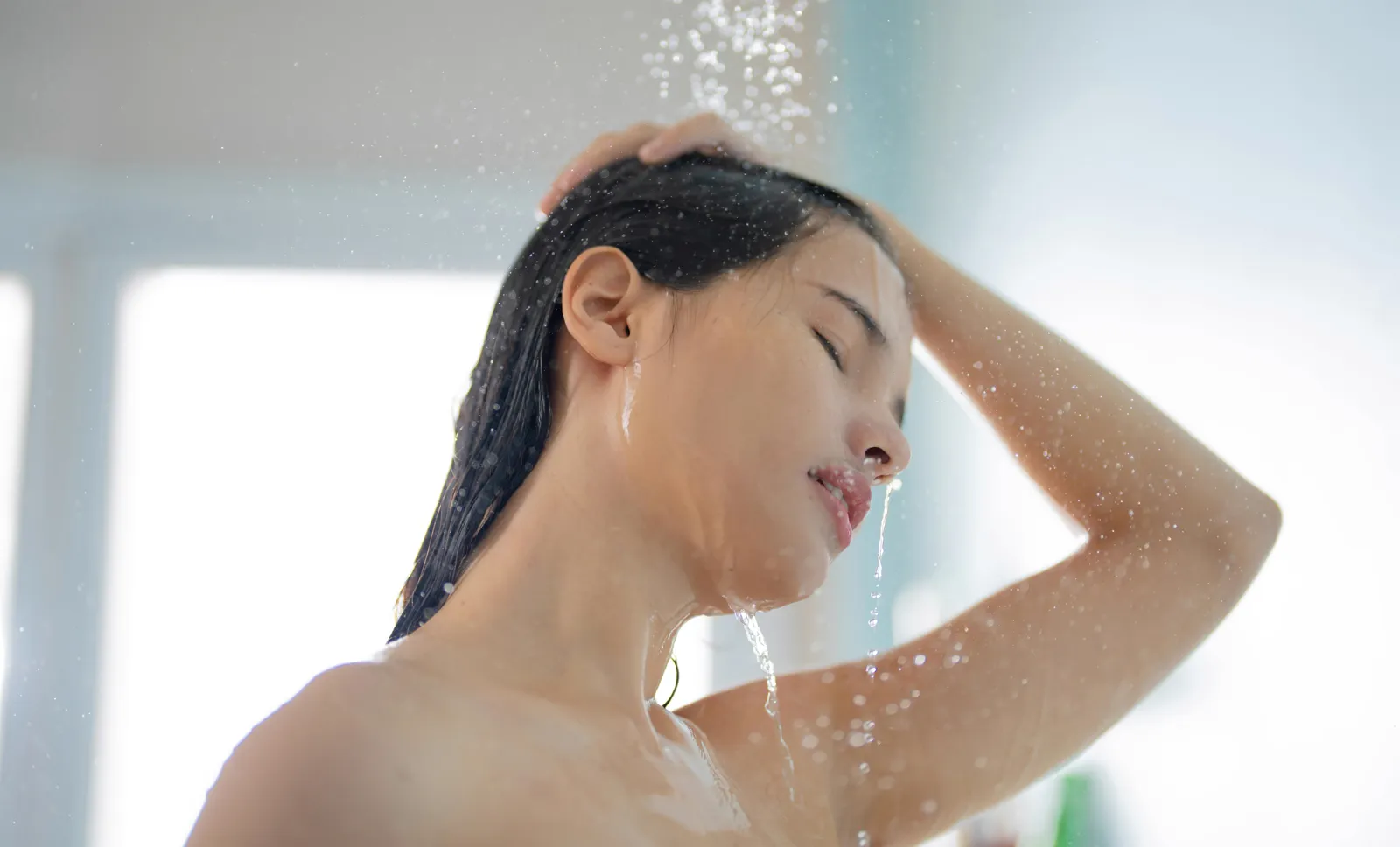 Woman rinsing her hair in the shower — shower water quality affects skin and hair health every single day