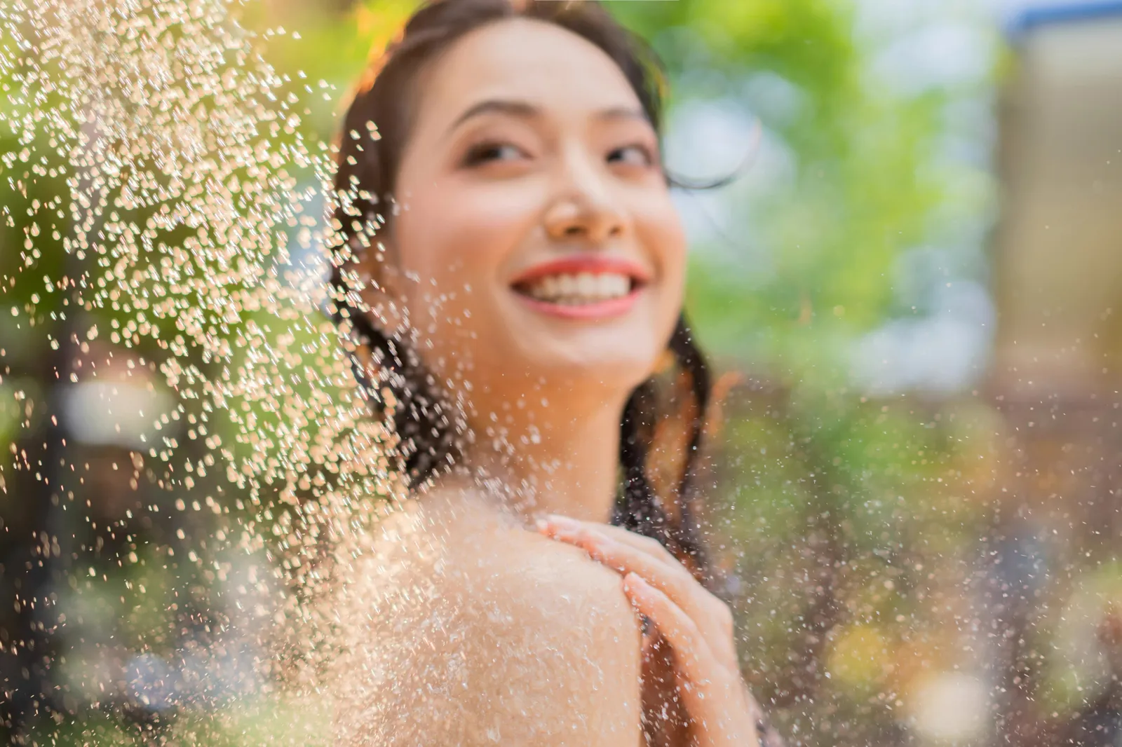 Woman smiling in a fresh outdoor shower spray, enjoying clean, chlorine-free water on her skin and hair