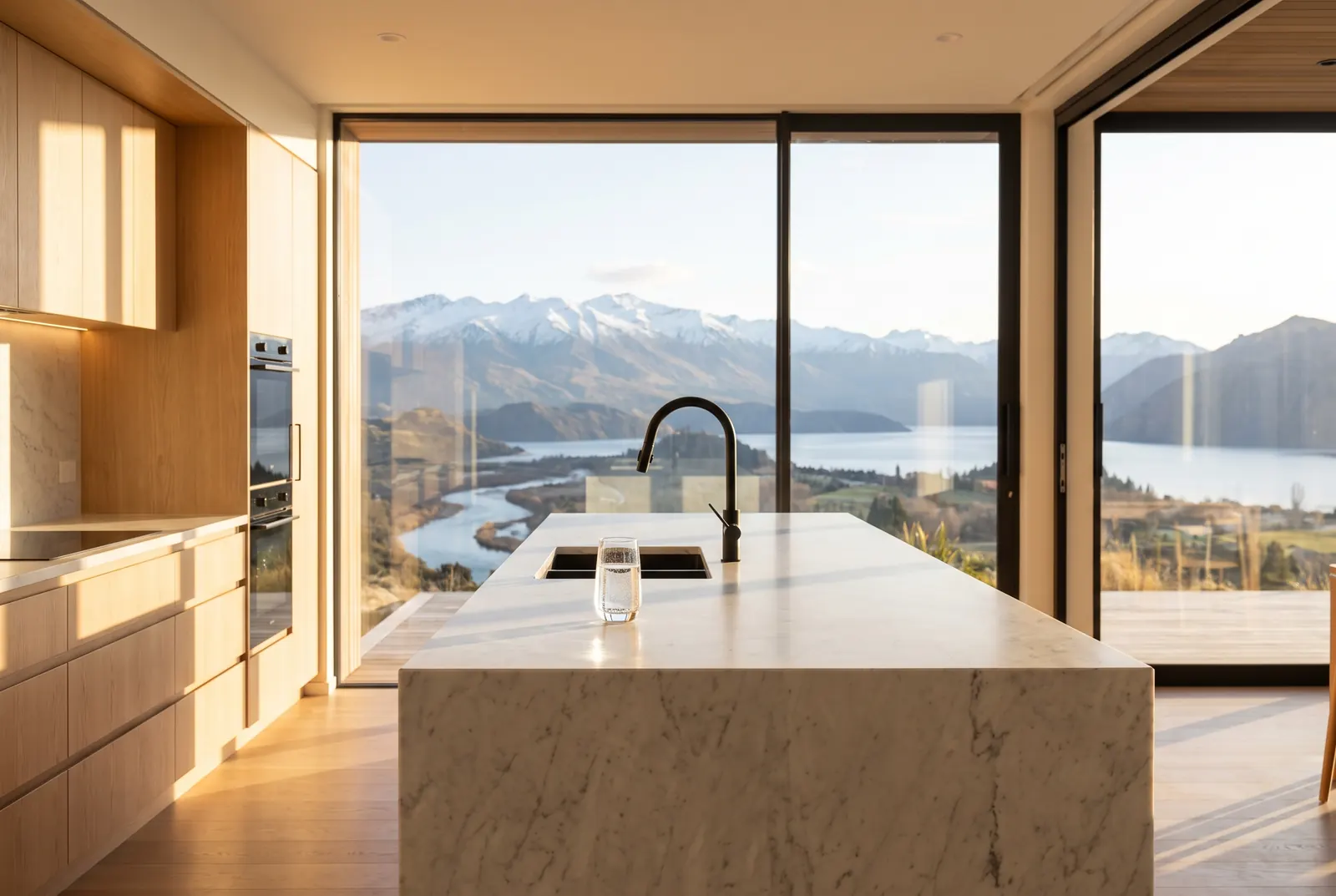 A bright modern luxury kitchen at golden hour with mountain views and a fresh glass of filtered water on the marble island